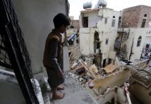 A Yemeni child looks at the ruins of war from a dilapidate structure