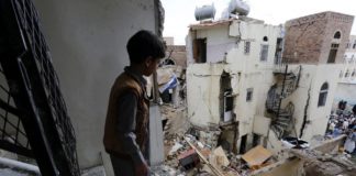 A Yemeni child looks at the ruins of war from a dilapidate structure